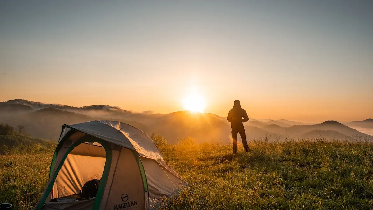 Sunrise: A man outside his tent looking towards the sun as it rises in the horizon